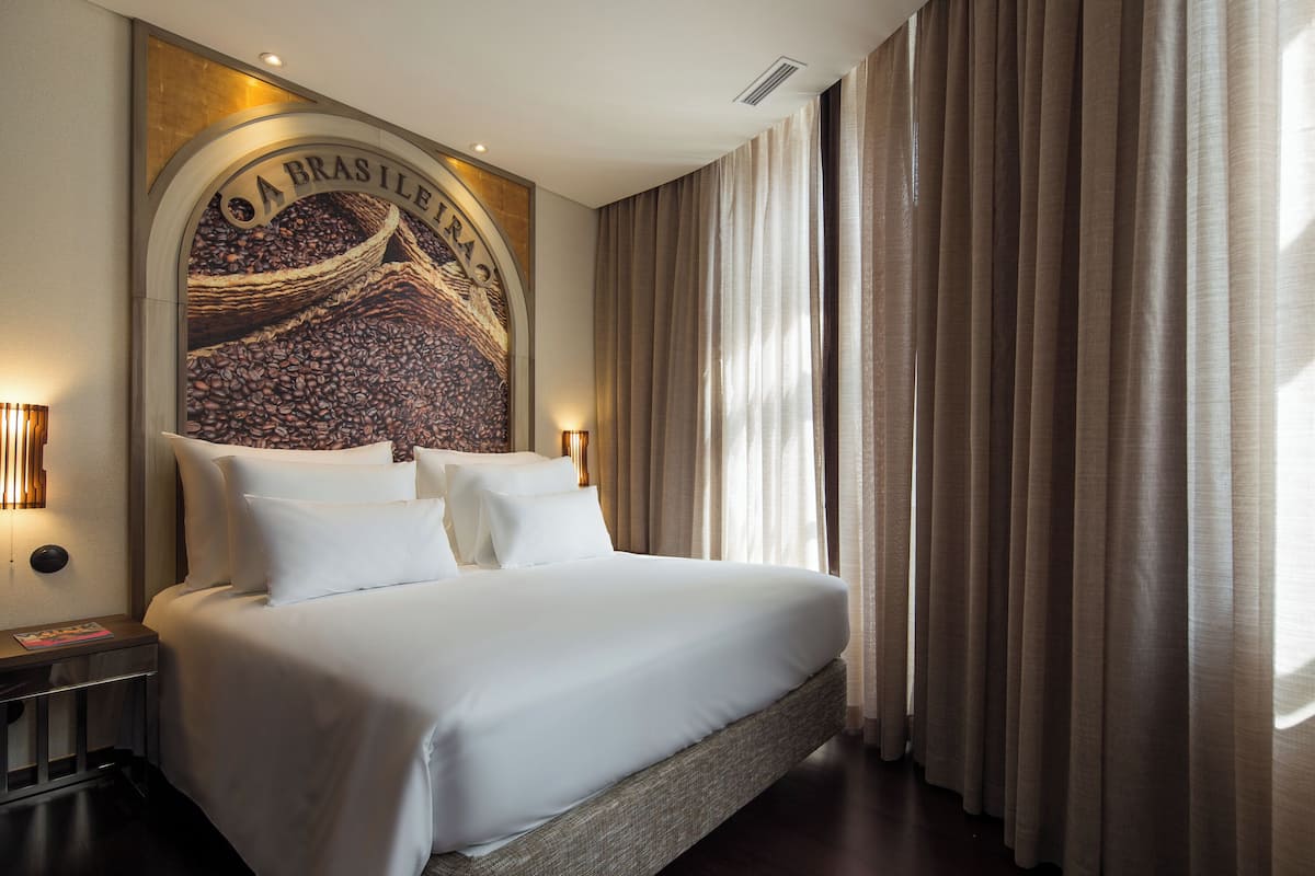 Habitación de hotel con una cama grande, cabecera con un mural de granos de café y vista a la ciudad.