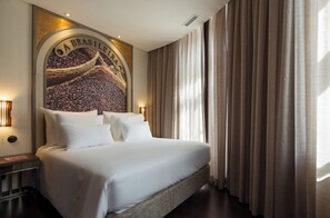 Une chambre d’hôtel avec un grand lit, une tête de lit ornée d’une fresque représentant des grains de café et une vue sur la ville.