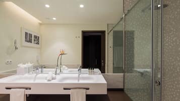 A modern bathroom with a large white sink, a glass shower enclosure, and a framed photograph on the wall.