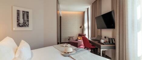 A hotel room with a bed, a desk with a laptop, a television, and a framed picture on the wall.