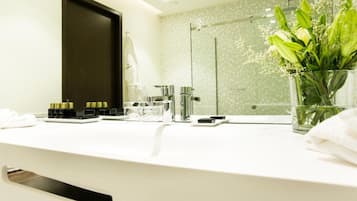 Un baño moderno con un tocador blanco, cabina de ducha con mampara de vidrio y un jarrón de flores sobre la encimera.