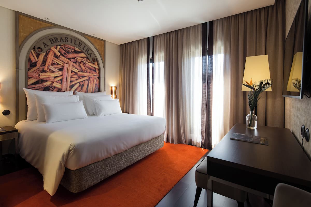 Habitación de hotel con una cama grande, un escritorio, una lámpara y un televisor de pared.