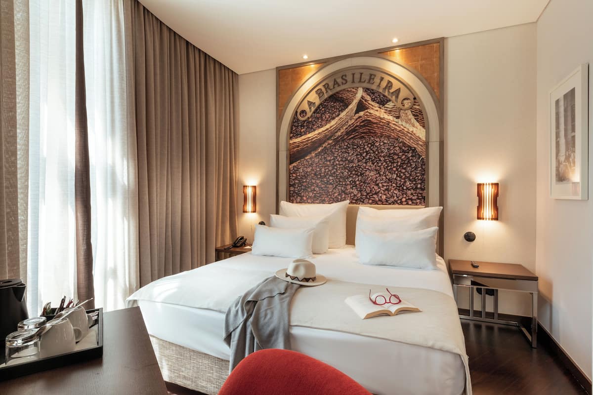 Habitación de hotel con una cama grande, una mesita de noche, una silla roja y una pared con un arco decorativo.