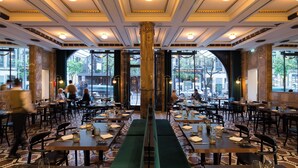 A restaurant with a central column, multiple tables, and a view of the street through large windows.