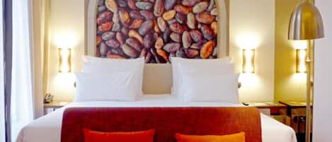 A hotel room with a large bed, two pillows, a headboard, and a wall-mounted artwork featuring coffee beans.