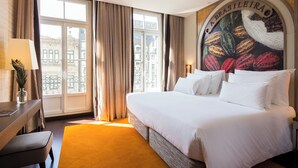 Een hotelkamer met een groot bed, een bureau en uitzicht op de stad door grote ramen.