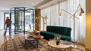 Een moderne lobby met een groene bank, twee ronde tafels met drankjes, een glazen scheidingswand en een groot raam met dunne gordijnen.