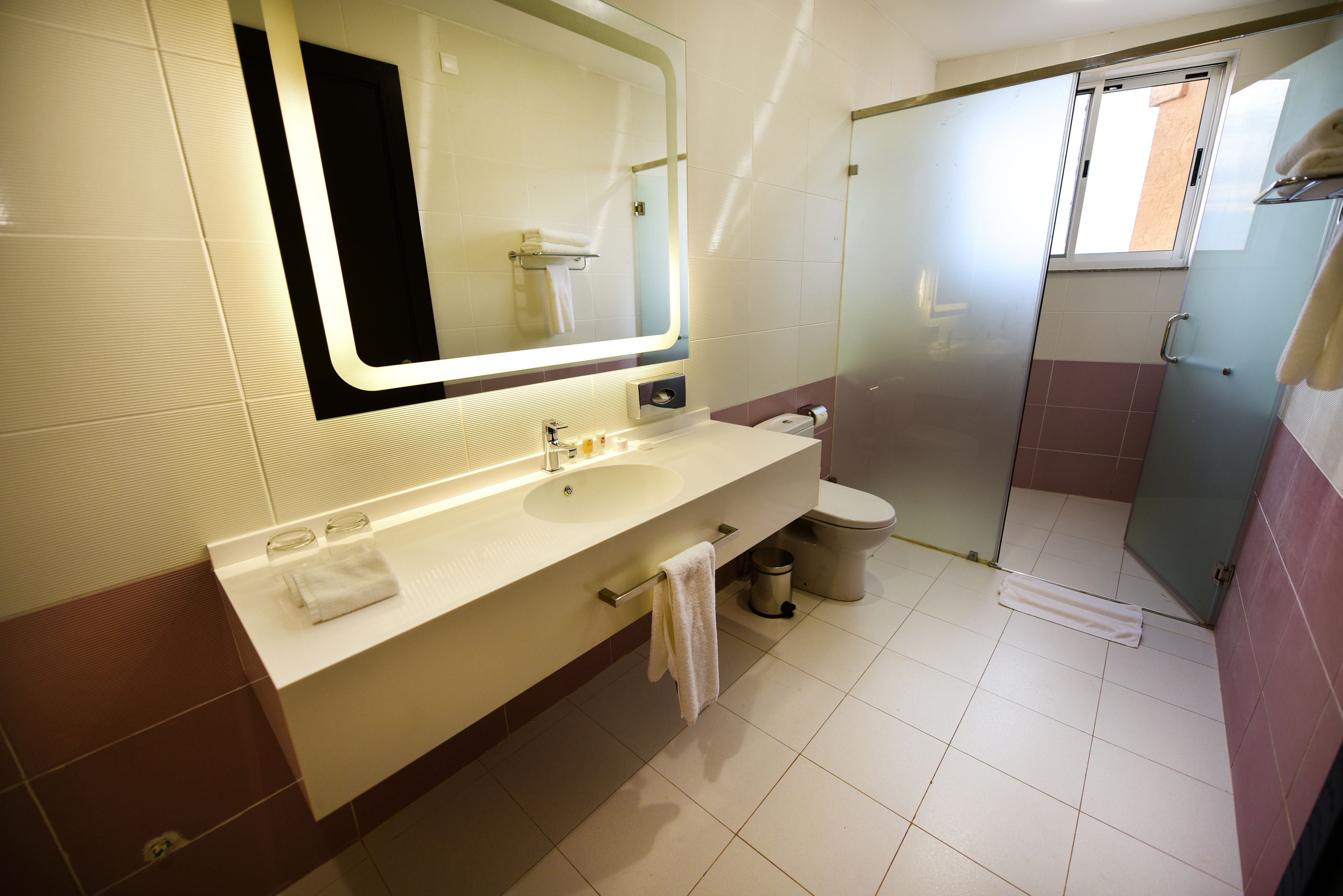 Ein Badezimmer mit großem Spiegel, Waschbecken, Toilette und Duschbereich.