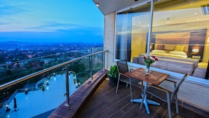 A balcony with a dining table and chairs, a view of a cityscape, and a bedroom with a bed and a vase of flowers. - Protea Hotel by Marriott Kampala Skyz (Kampala)