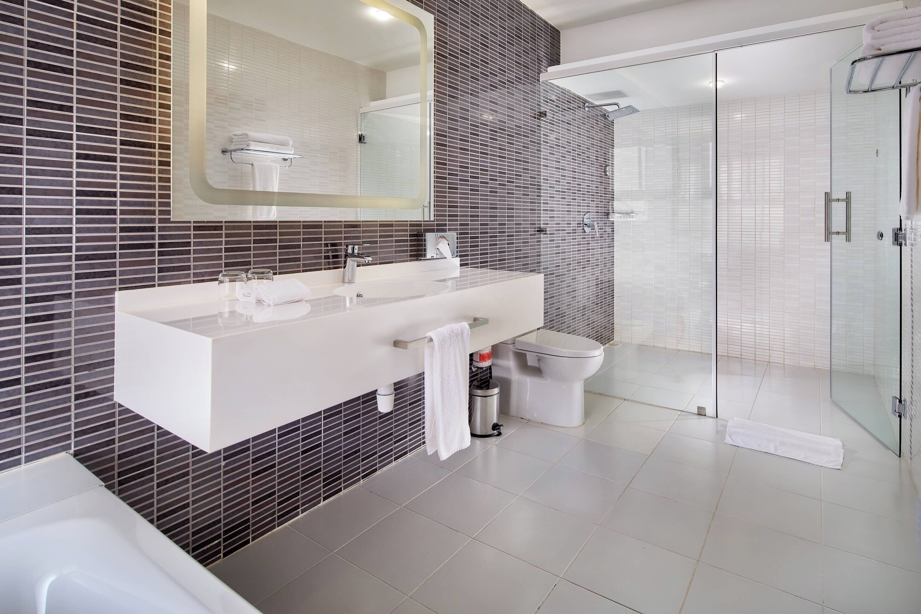 A modern bathroom with a large mirror, a white sink, and a glass-enclosed shower.