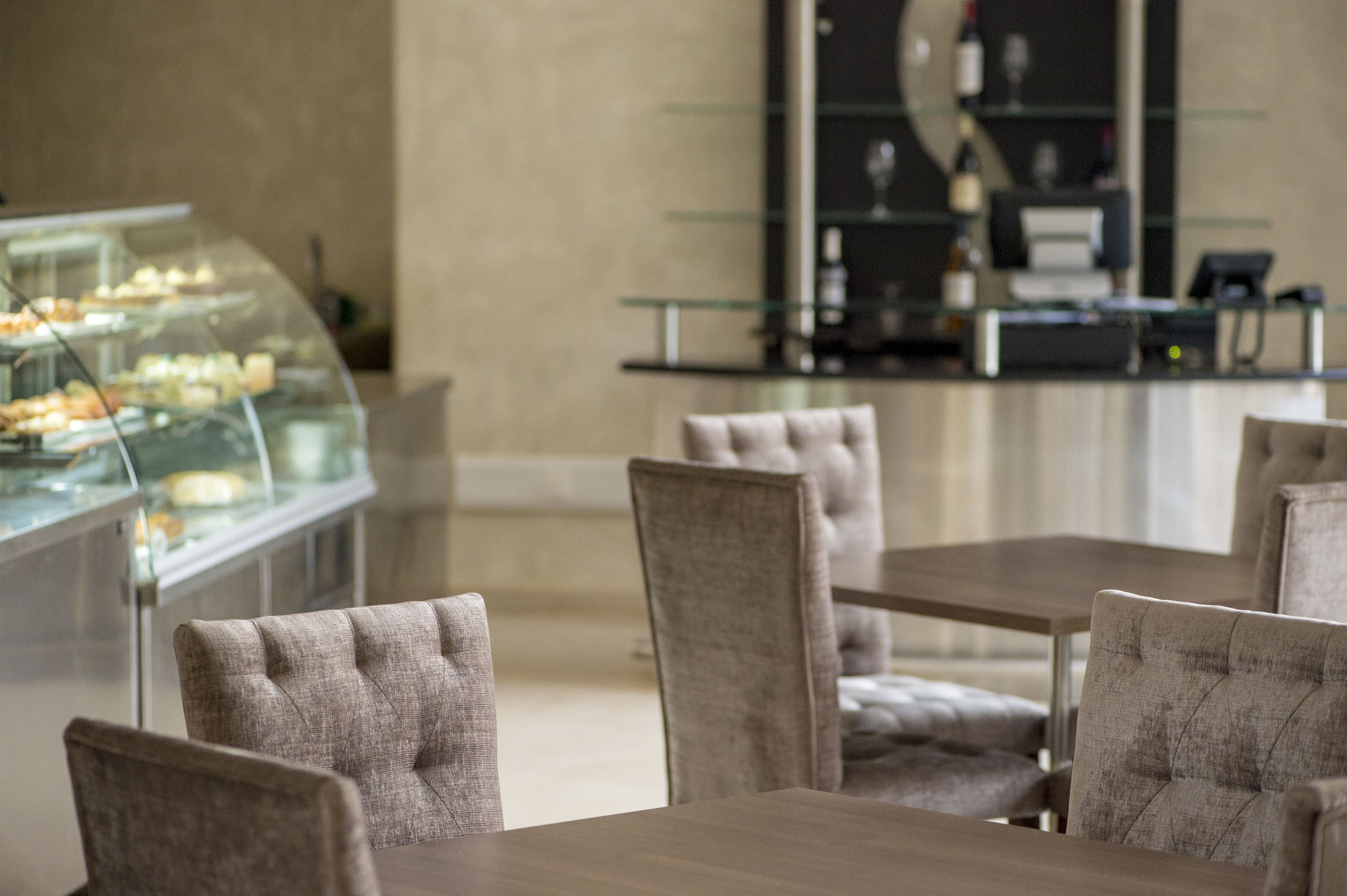 A dining area with cushioned chairs and a glass display case with pastries.