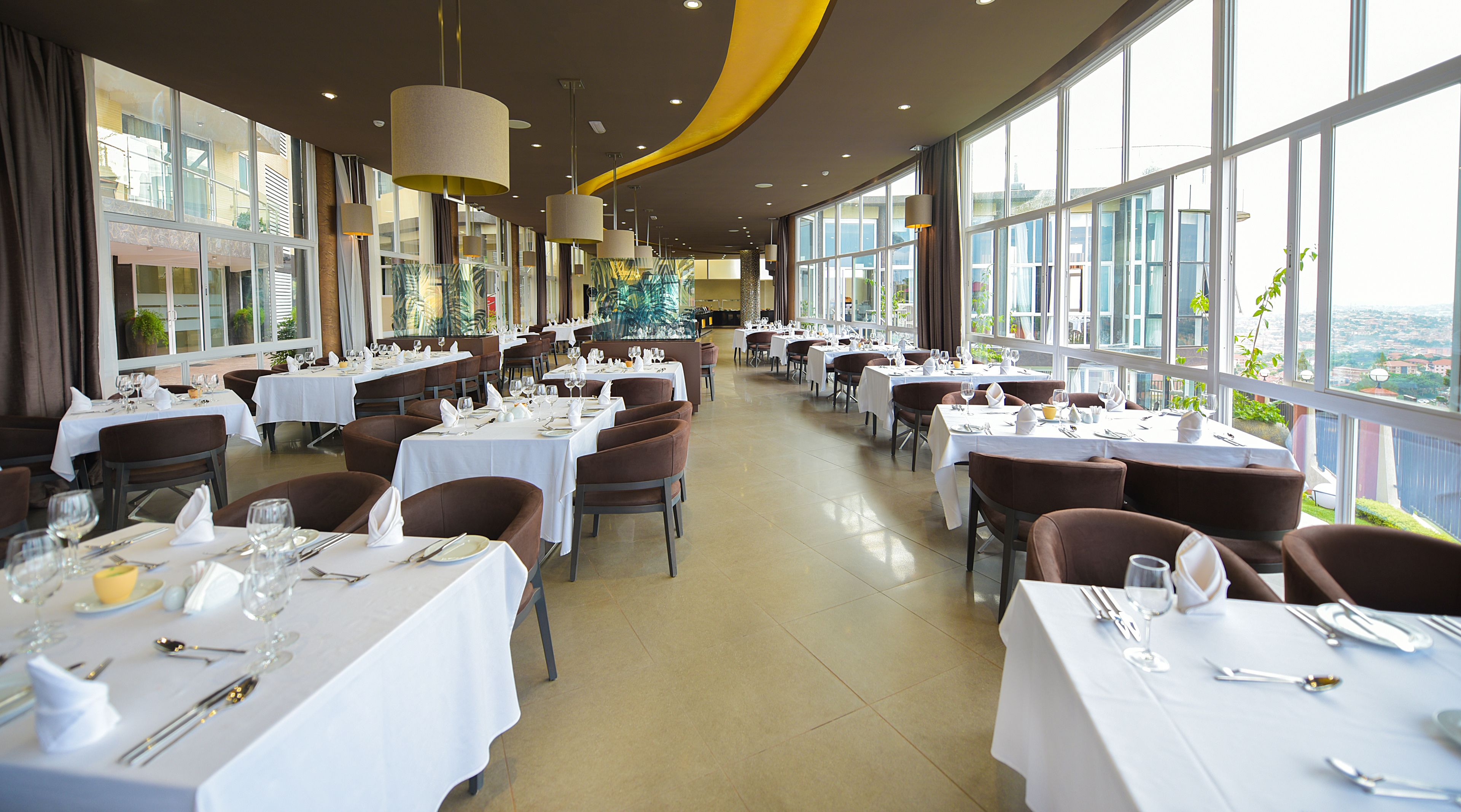 Ein geräumiges Restaurant mit mehreren gedeckten Tischen, großen Fenstern mit Blick und modernen Leuchten.