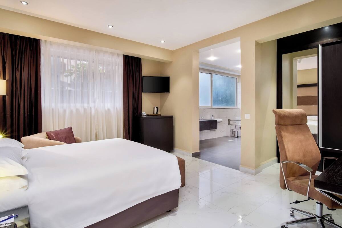 Une chambre d’hôtel avec un lit, un bureau, une chaise, une télévision et une salle de bain visible à travers une porte ouverte.