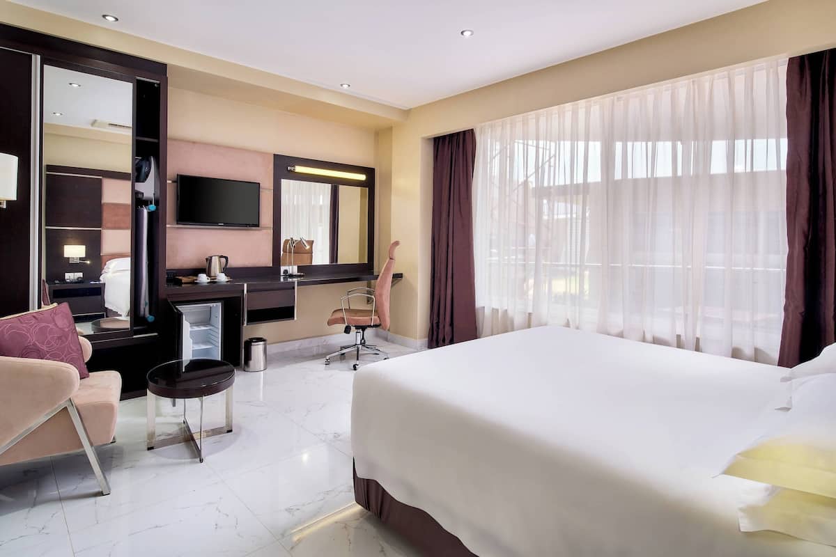 Une chambre d’hôtel avec un grand lit, un bureau avec une chaise, une télévision et un miroir.