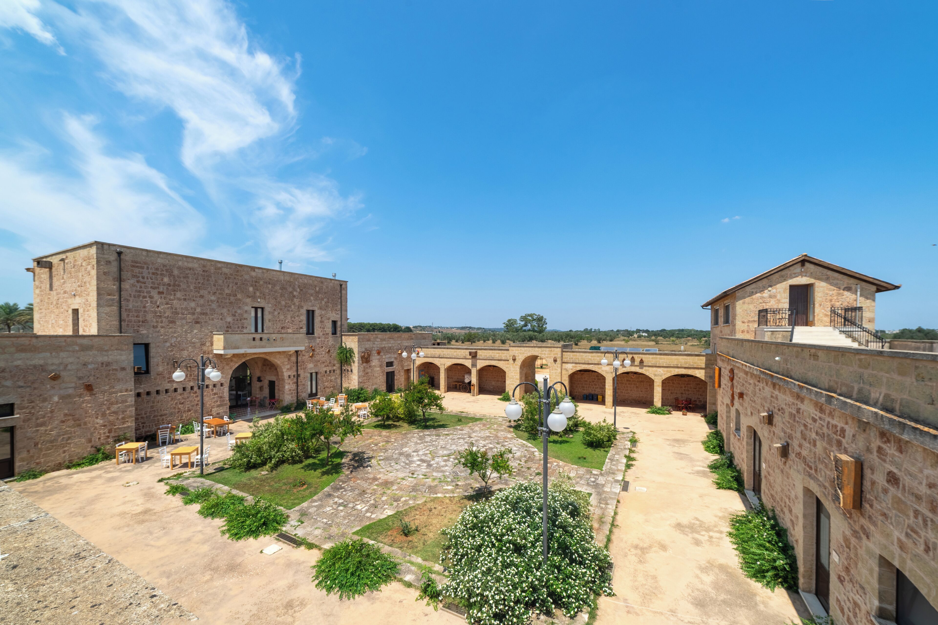 A courtyard with stone buildings, outdoor seating, and a clear sky.