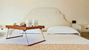 Un lit bien fait, avec une tête de lit blanche, une table de chevet sur laquelle se trouve un plateau avec deux tasses et un biscuit, et un tapis à motifs.
