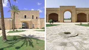 Un bâtiment à la façade en pierre et à l’entrée en arc de cercle, entouré d’une cour plantée de palmiers et dotée d’un chemin pavé.