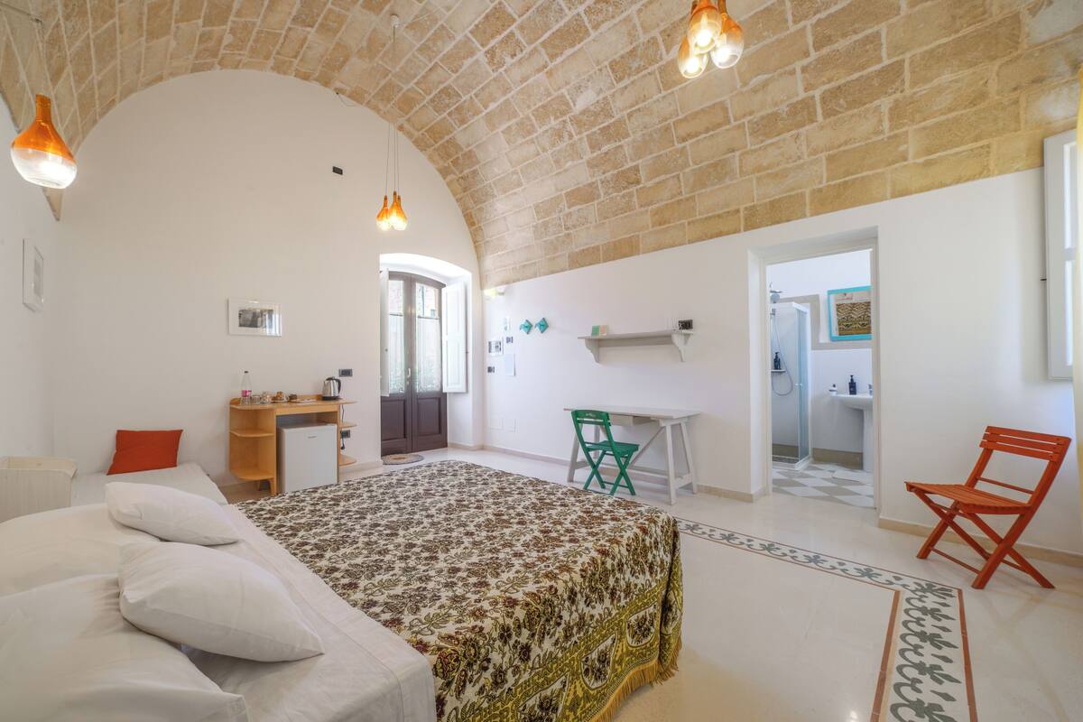 Une chambre avec un lit, un bureau et une chaise, une salle de bain et un coin cuisine.
