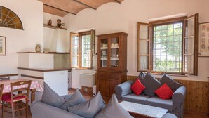 A cozy living room with a grey sofa, a wooden cabinet, and a dining table with a red tablecloth. - Agriturismo il Poggiarello (Siena)