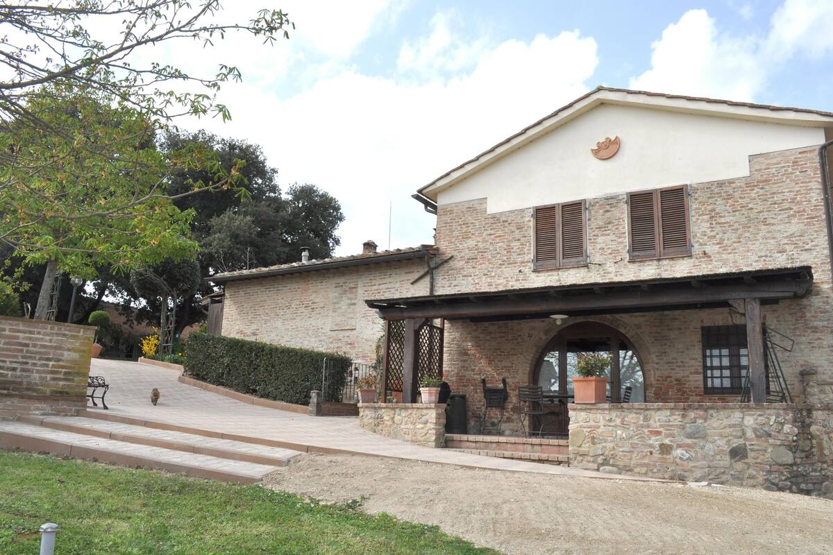 A two-story building with a stone facade, a covered patio area, and a small garden with potted plants.