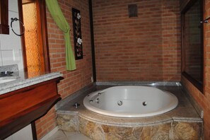 Un baño con una bañera grande, un tocador de madera y una pared de ladrillo.