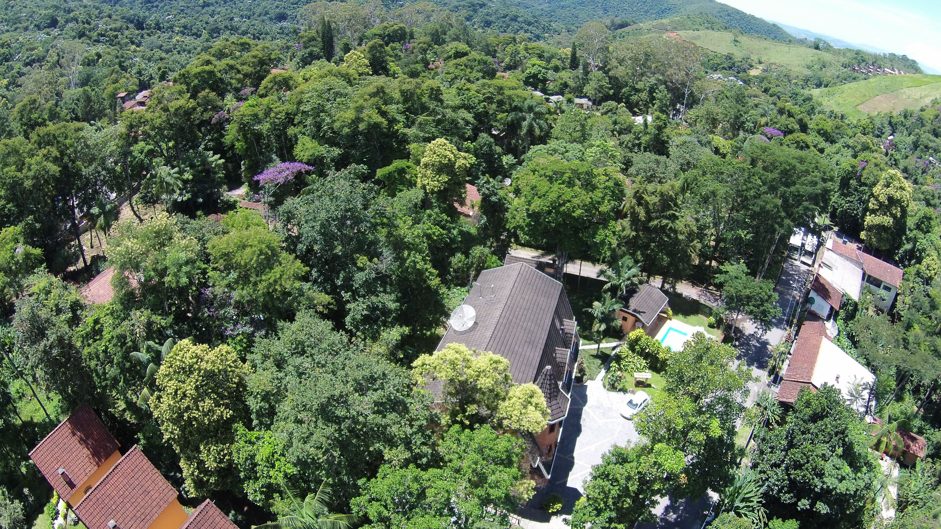 An aerial view of a residential area with houses surrounded by dense greenery and hills in the background.