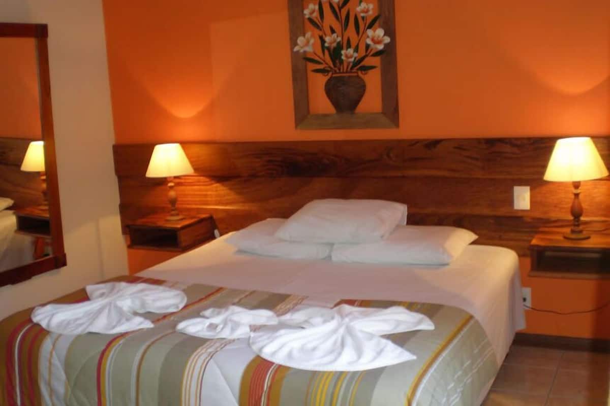 Ein Hotelzimmer mit einem Bett, zwei Nachttischen, einem Spiegel und einem Blumenbild an der Wand.