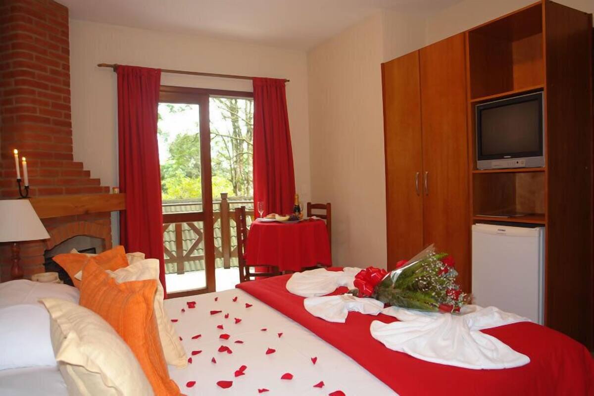 Ein Hotelzimmer mit Bett, Fernseher, Kamin und einem Balkon mit roten Vorhängen.