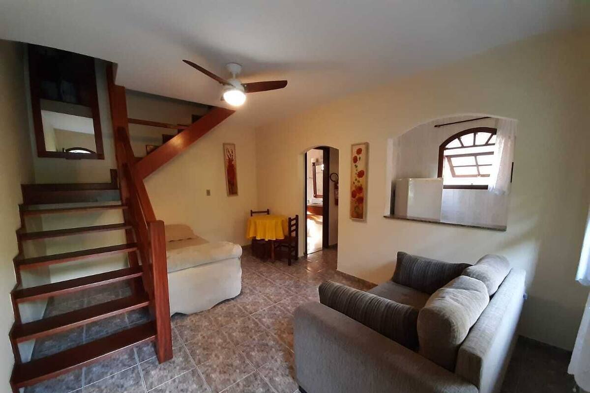 Ein Wohnzimmer mit Treppe, einer Couch, einem Esstisch mit Stühlen und einem Deckenventilator.