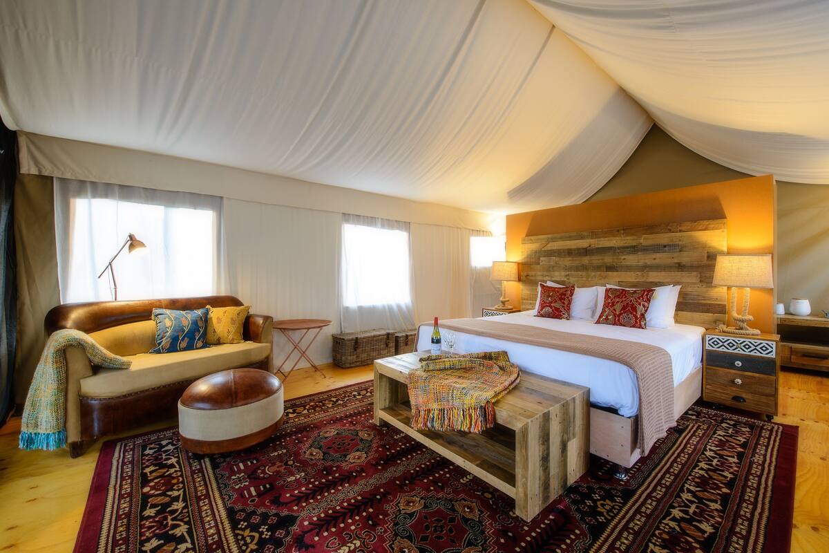 A spacious bedroom with a large bed, a sofa, a wooden coffee table, and a patterned rug.