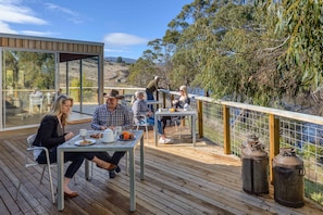 A wooden deck with outdoor seating, a glass enclosure, and a view of a natural landscape.
