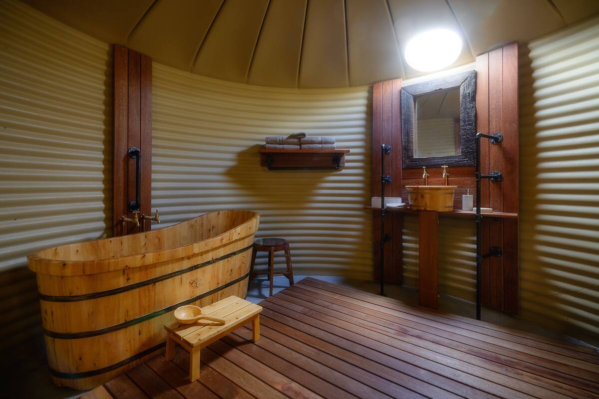 A sauna room with a wooden tub, a wooden bench, a shelf with towels, and a wooden cabinet with a mirror.