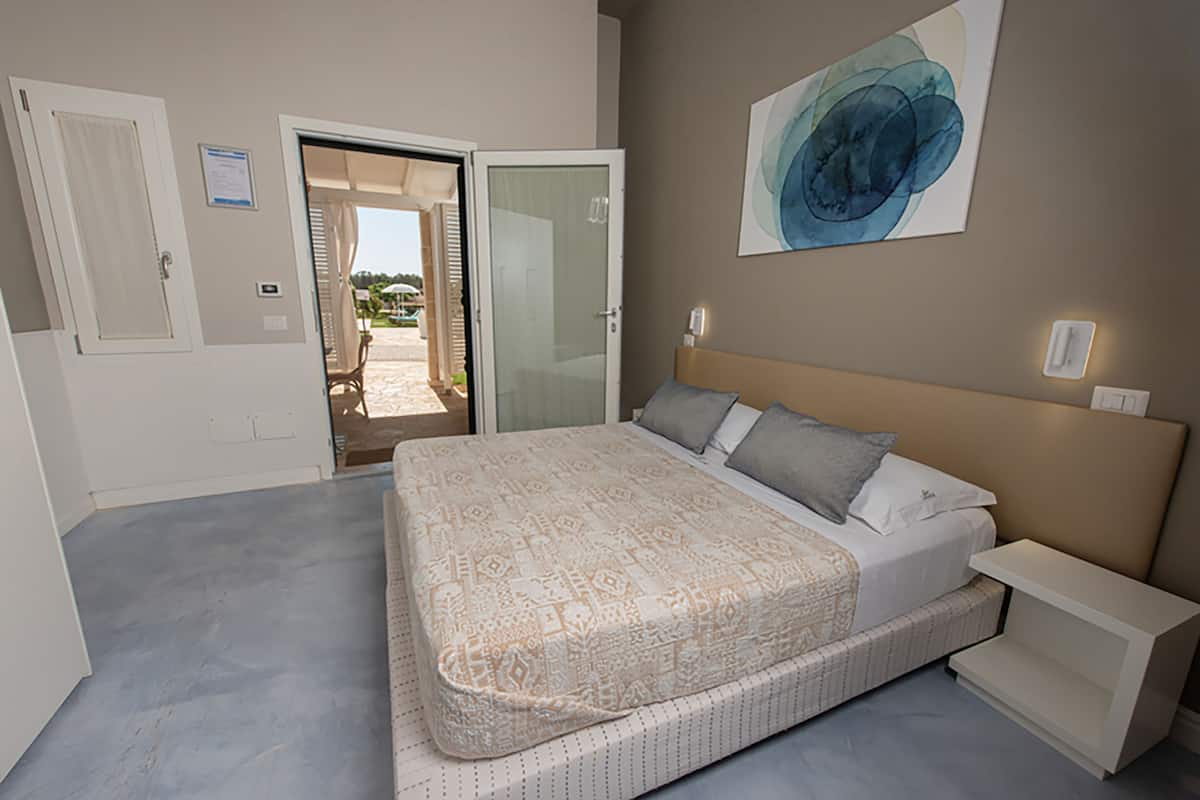 Ein Schlafzimmer mit Bett, Nachttisch, einer Tür und Blick ins Freie.