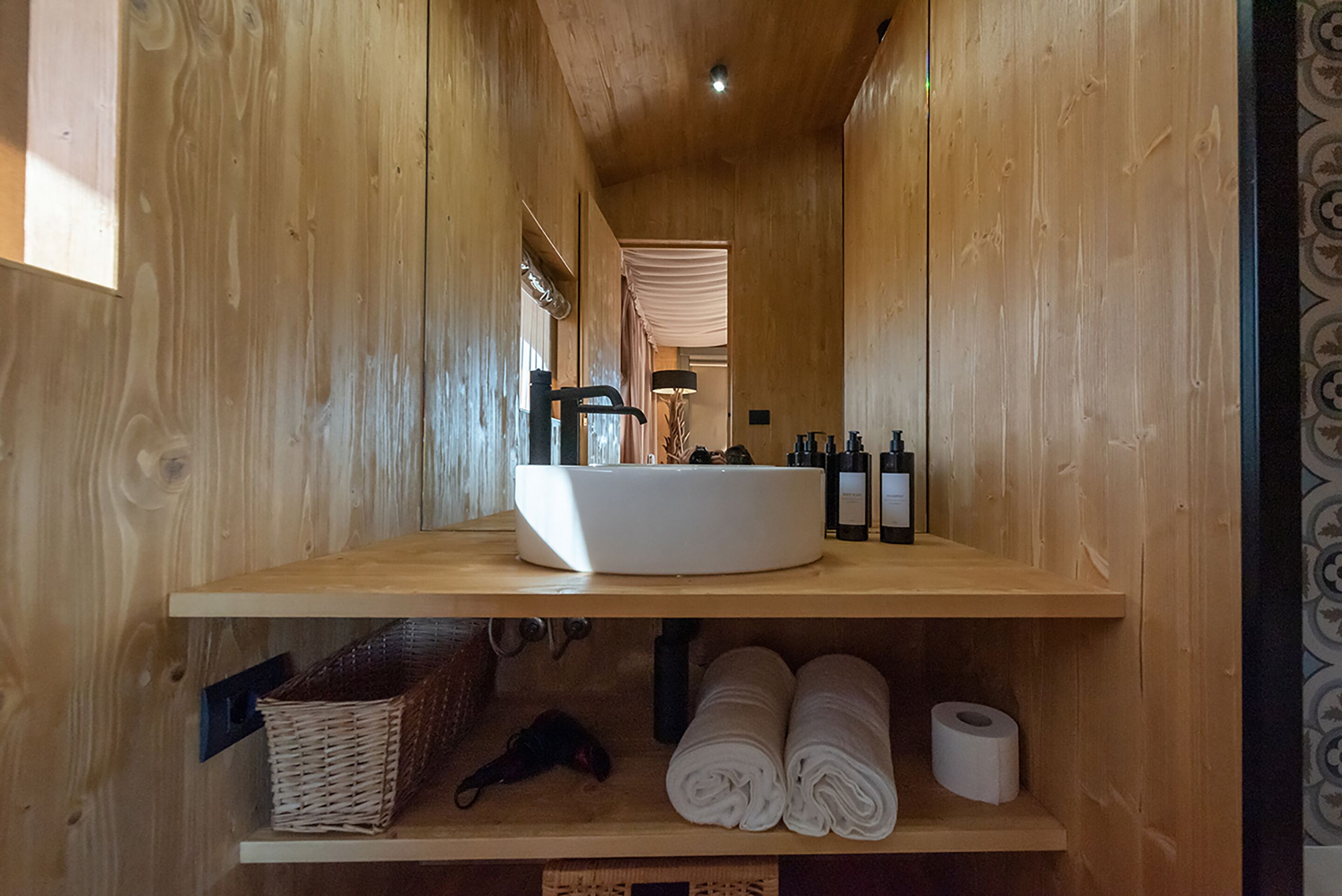 A wooden interior with a white sink, shelves with toiletries, and a basket.