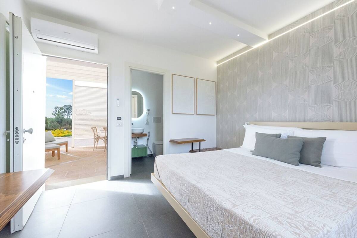 Ein modernes Schlafzimmer mit einem großen Bett, ein Badezimmer mit Spiegel und eine Terrasse mit Gartenmöbeln.