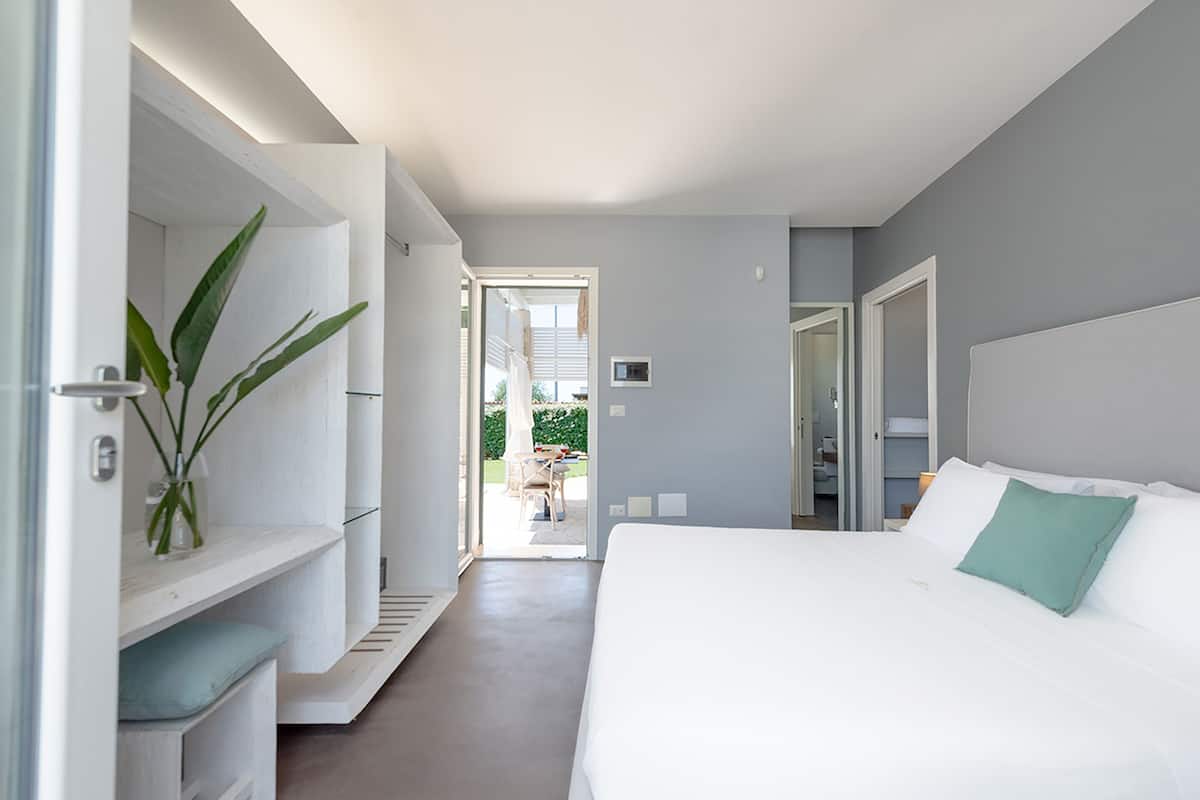 Ein modernes Hotelzimmer mit einem großen Bett, einer integrierten Garderobe und Blick ins Freie.