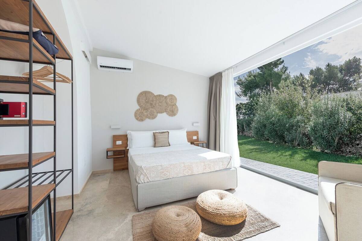 Ein modernes Schlafzimmer mit einem großen Bett, einer Holzhockerreie und Blick auf einen Garten.