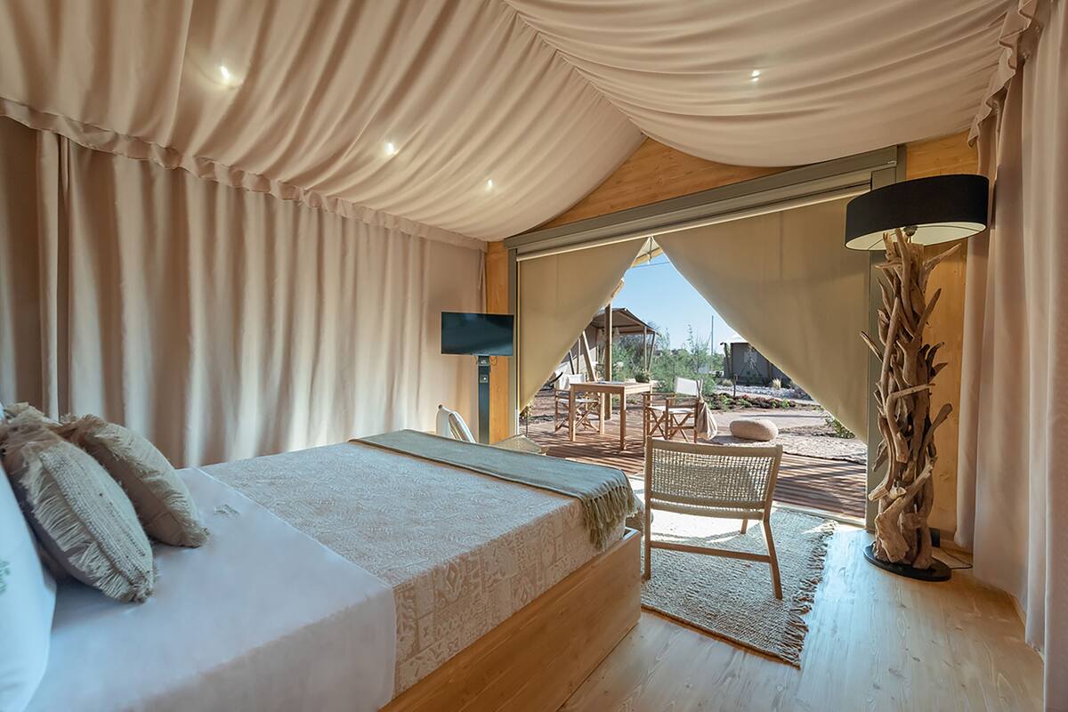 Ein Schlafzimmer mit einem großen Bett, einem Sessel, einem Tisch und Blick ins Freie.