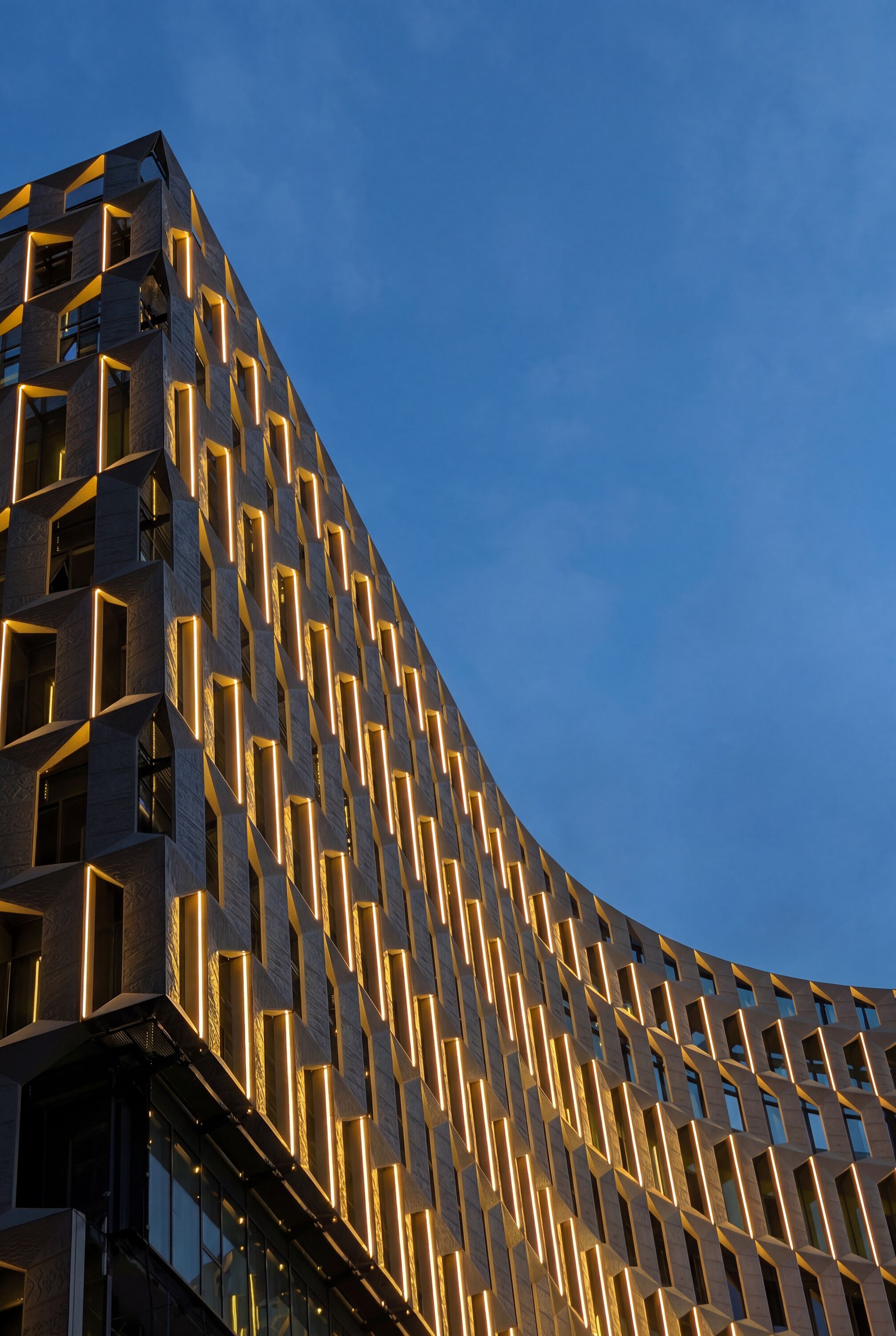 A modern building with a unique geometric facade and illuminated windows.