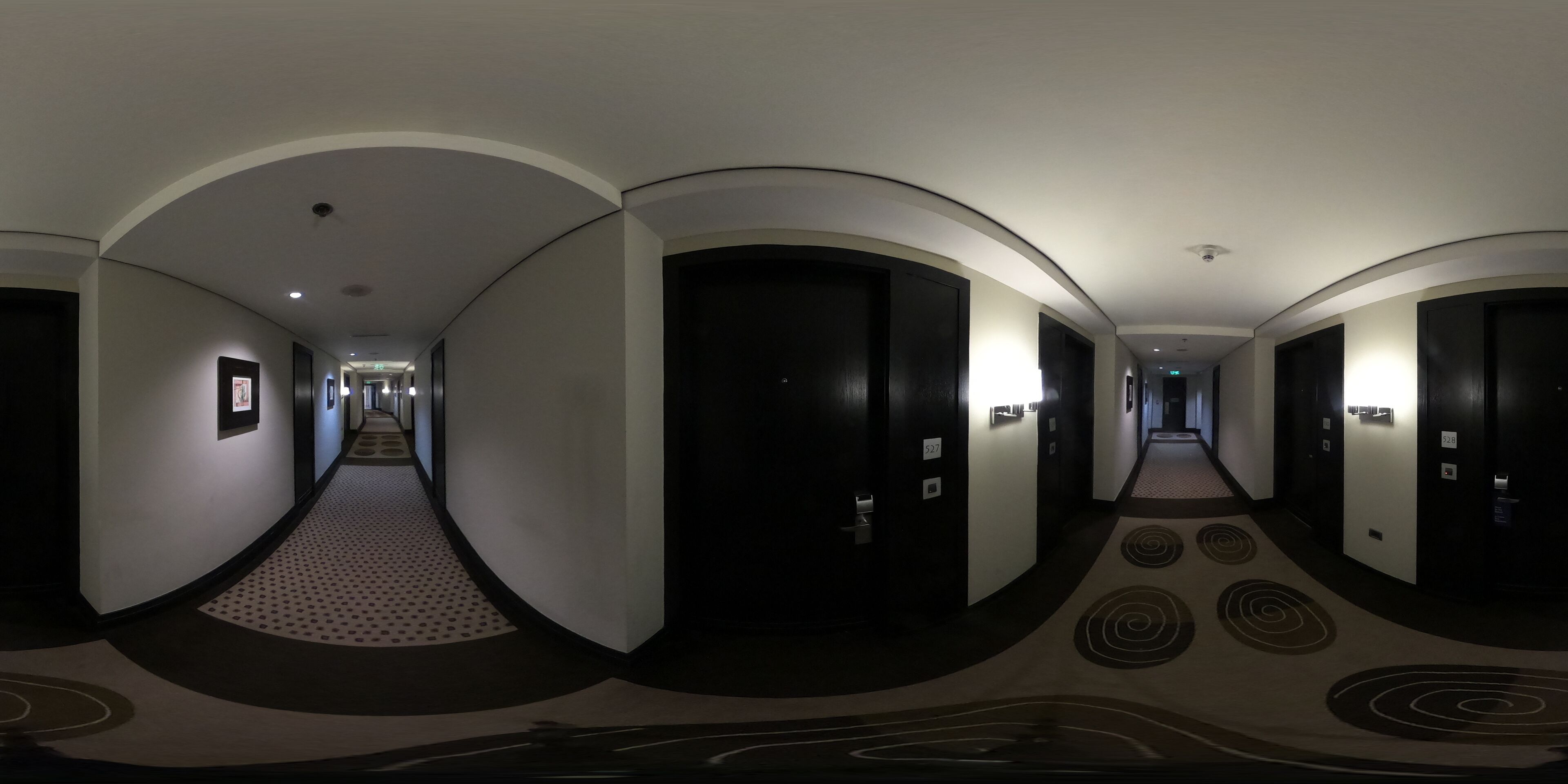 Corredor de hotel com teto curvo, portas escuras e carpete estampado.