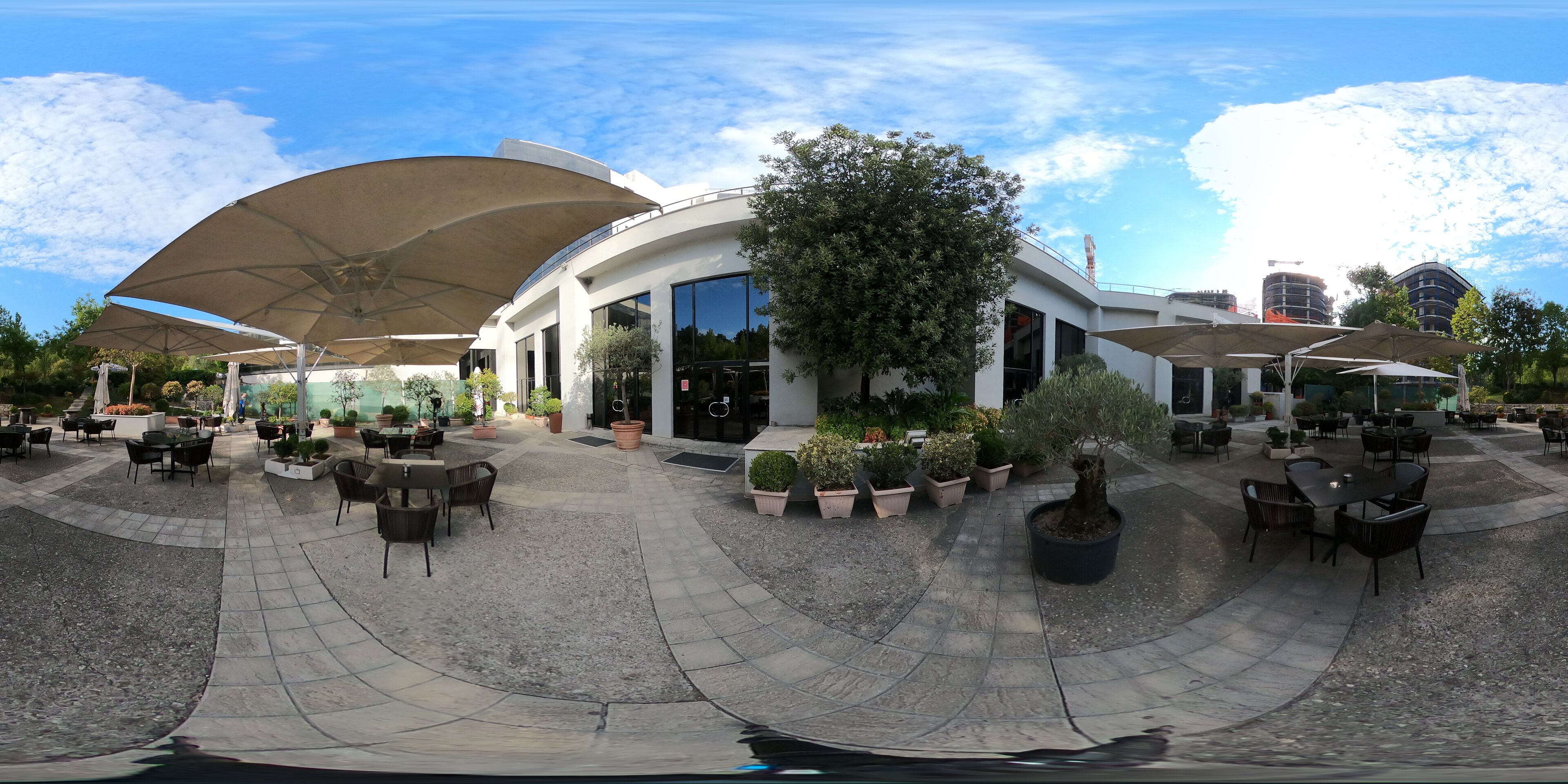 An outdoor patio area with tables and chairs, surrounded by potted plants and umbrellas.