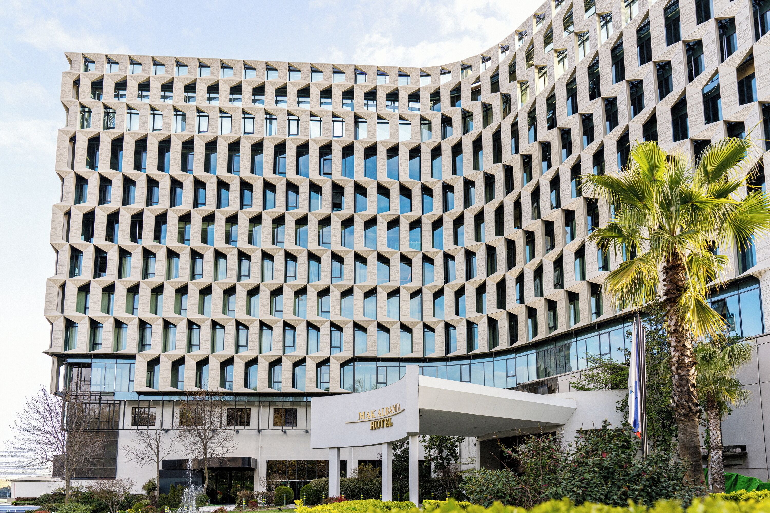 Un hotel moderno con fachada geométrica, una entrada destacada y un asta de bandera.