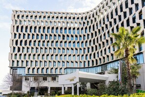 A modern hotel with a geometric facade, a prominent entrance, and a flagpole. - Mak Albania Hotel (Tirana)