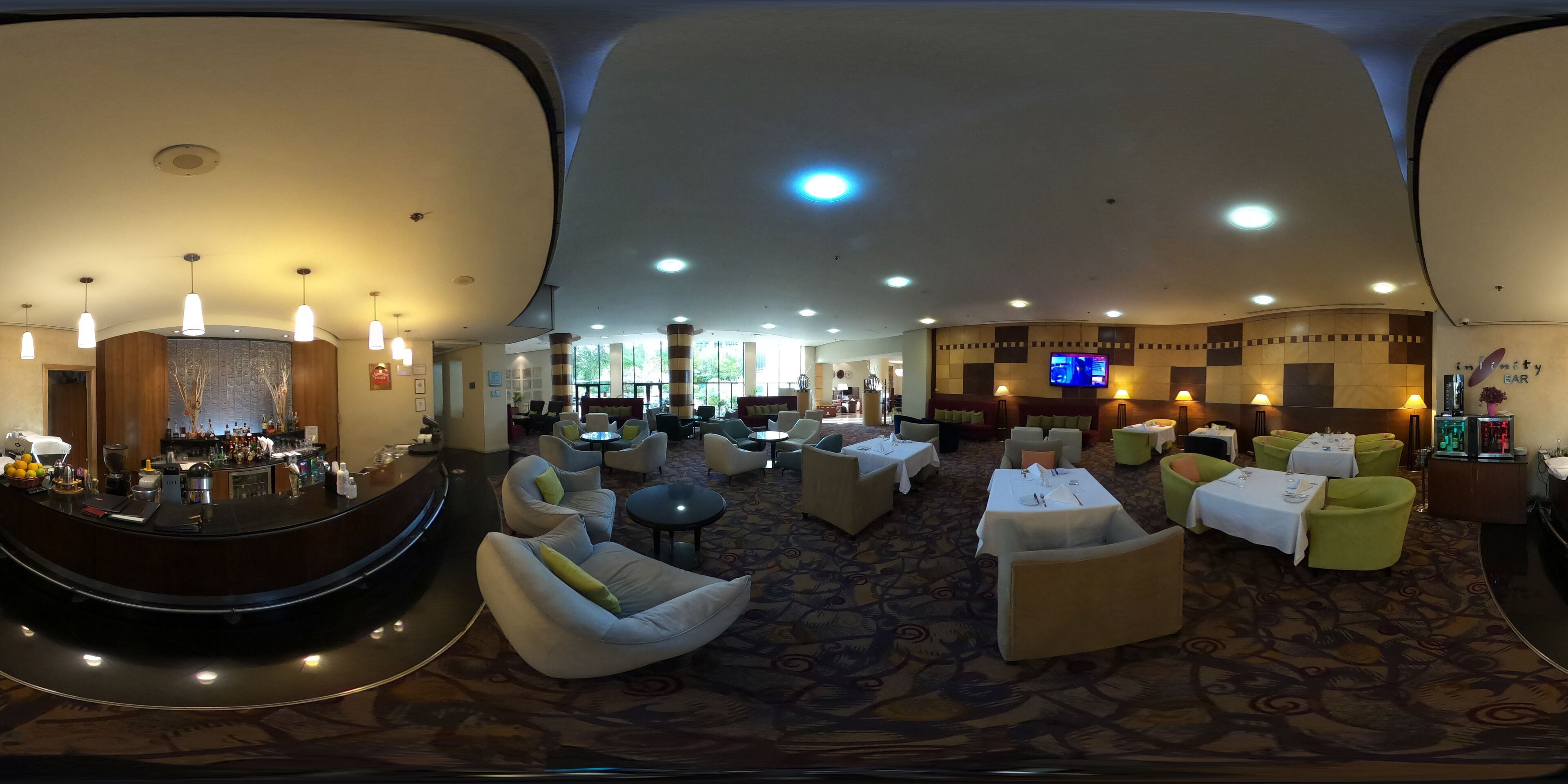 Un hall d’hôtel comprenant un bar, des espaces aménagés avec des sièges et un écran de télévision.