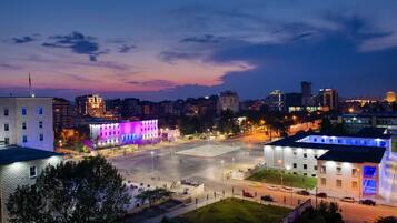 A cityscape at dusk with illuminated buildings, a large open plaza, and a mix of modern and traditional architecture.