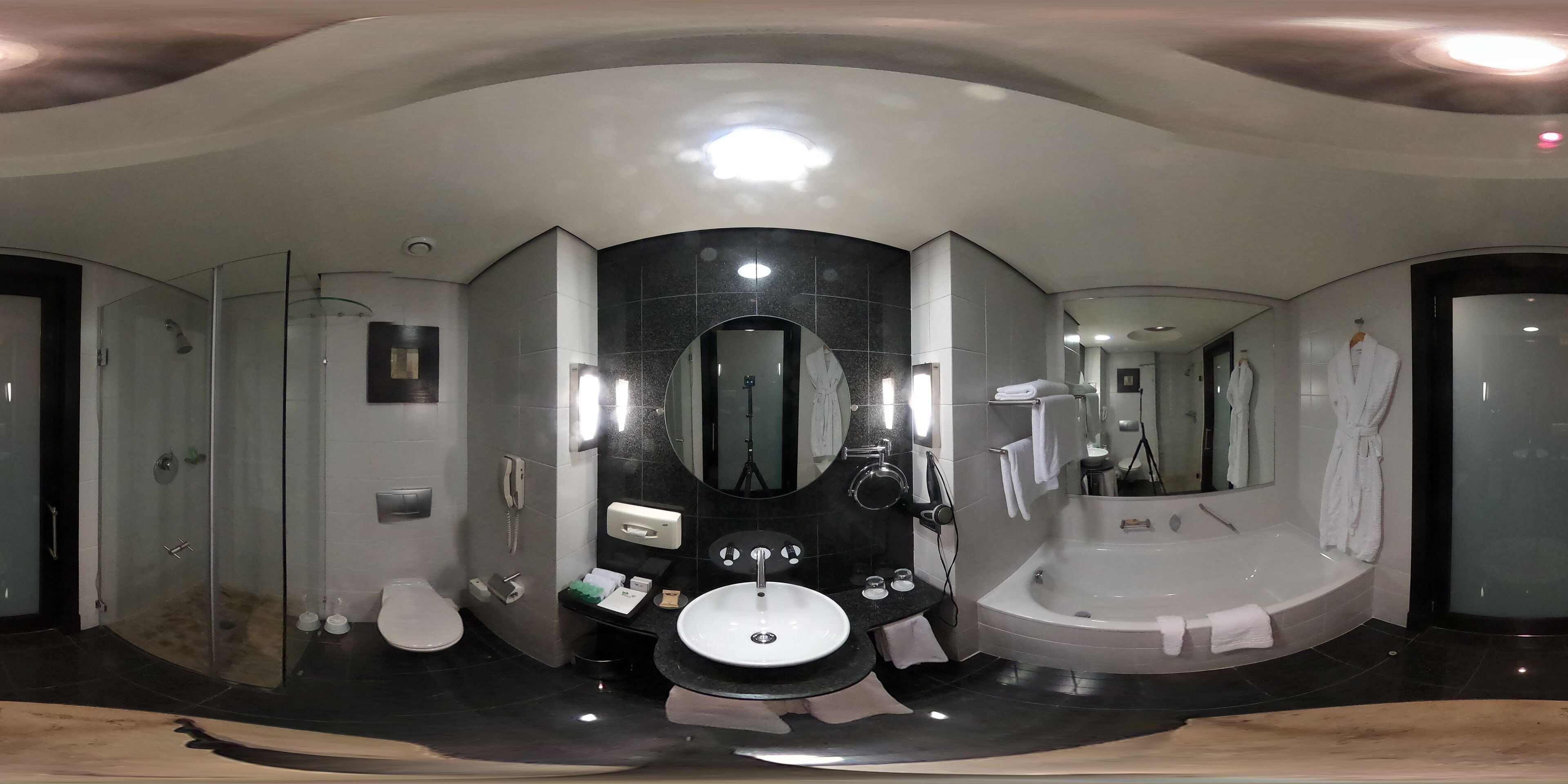 A modern bathroom with a large mirror, a bathtub, a toilet, and a sink.