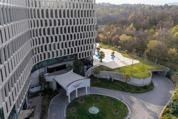 A modern hotel with a unique geometric facade, a central courtyard with a fountain, and a pool area surrounded by greenery. - Mak Albania Hotel (Tirana)