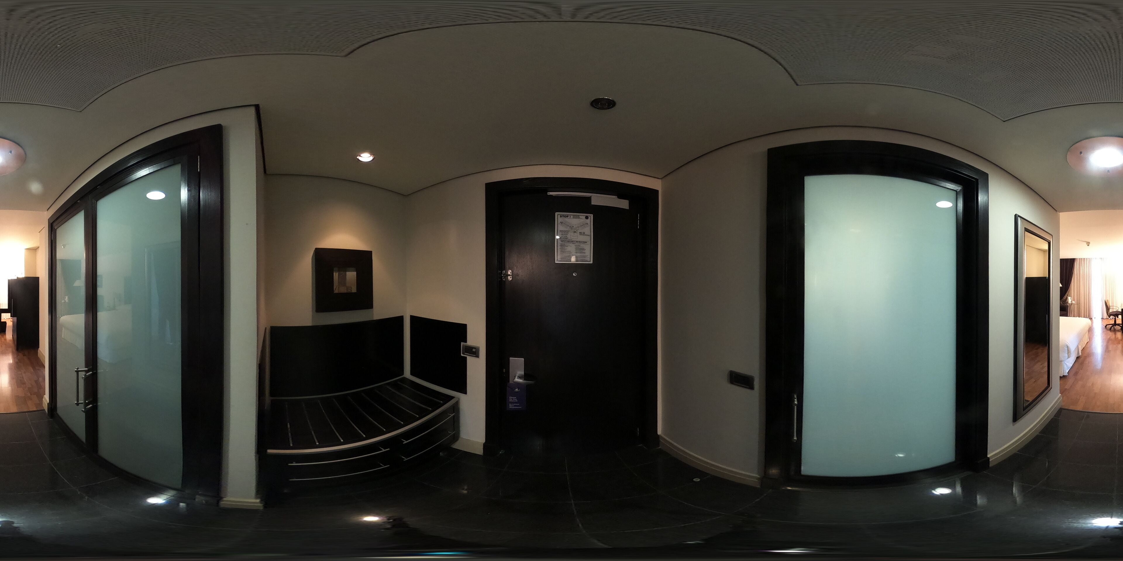 A modern hotel lobby with a curved ceiling, a reception desk, a staircase, and a glass door leading to a room.