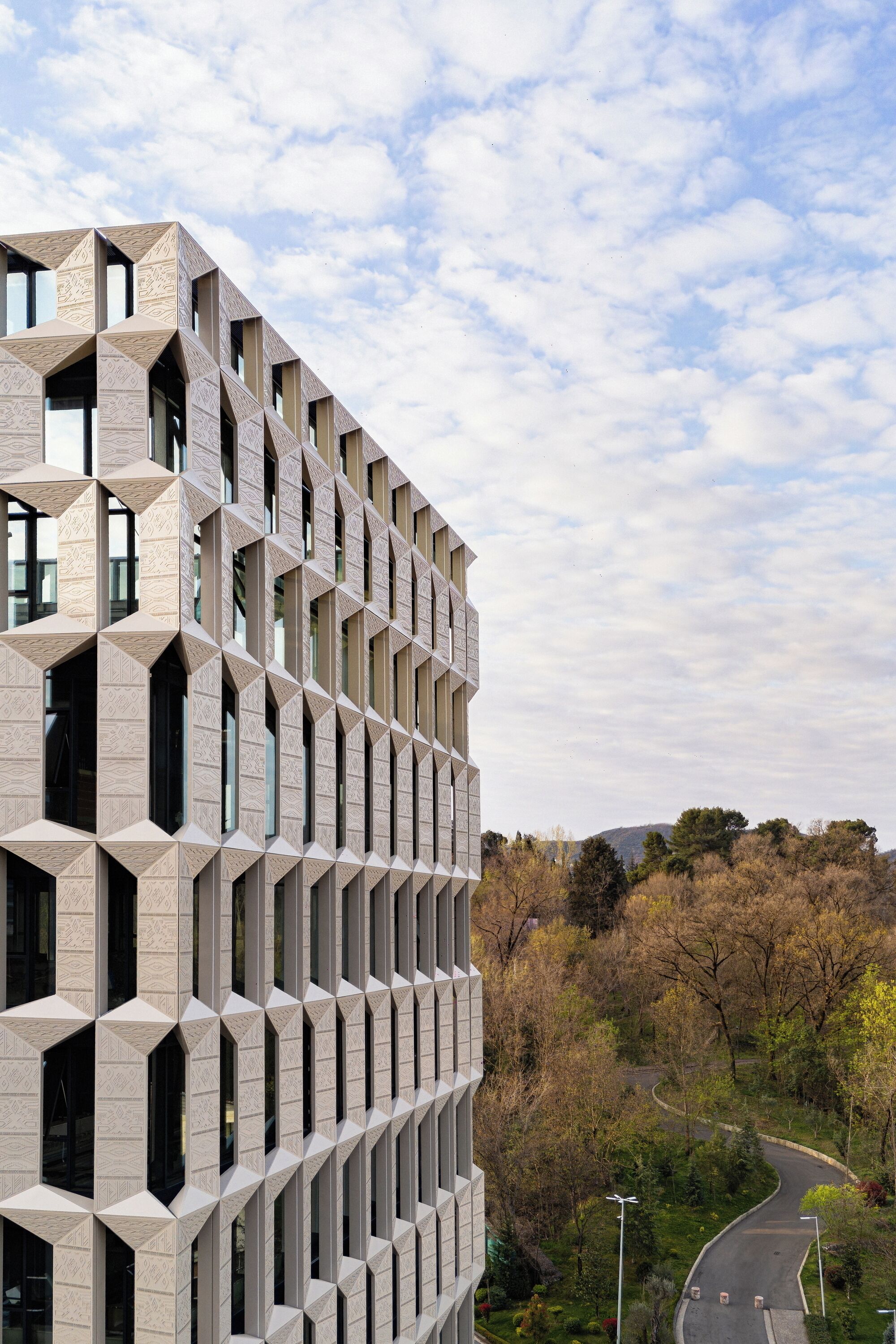 Un edificio moderno con fachada geométrica y una carretera curva al fondo.