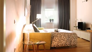 Habitación de hotel con cama, una mesita de noche con lámpara, televisor y ventana con cortinas.